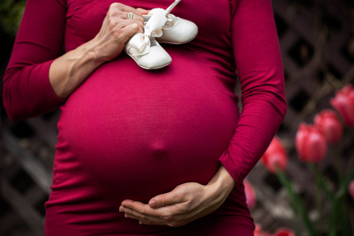 Pregnant woman holding baby shoes while planning a move before the baby arrives