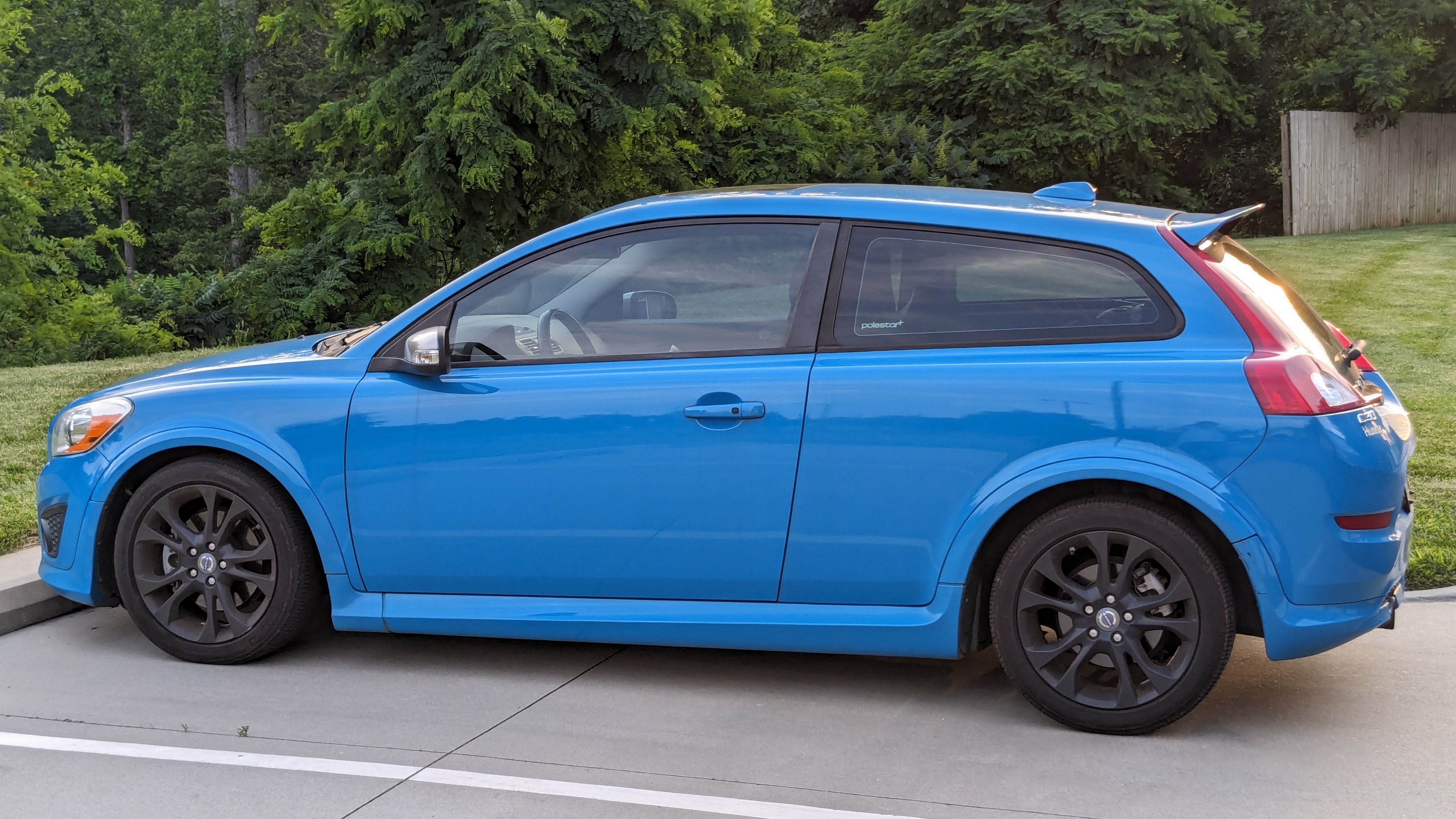 Side view of a blue car parked outdoors in a lush green setting, showcasing its vibrant color and sleek design.