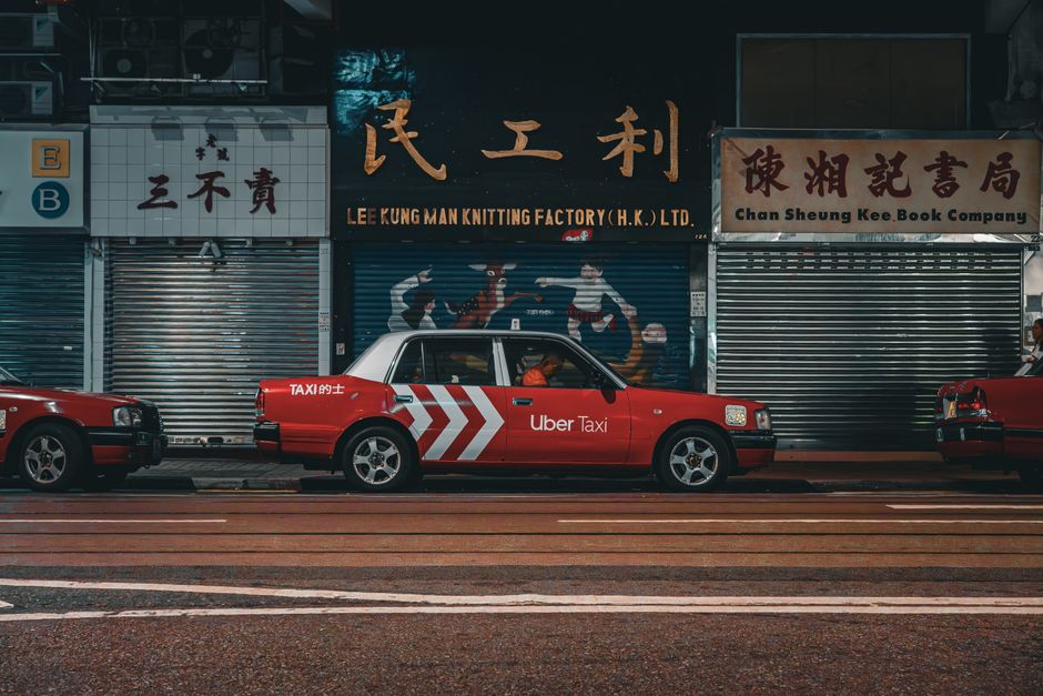 Red Uber Taxi parked on a vibrant Hong Kong city street at night.