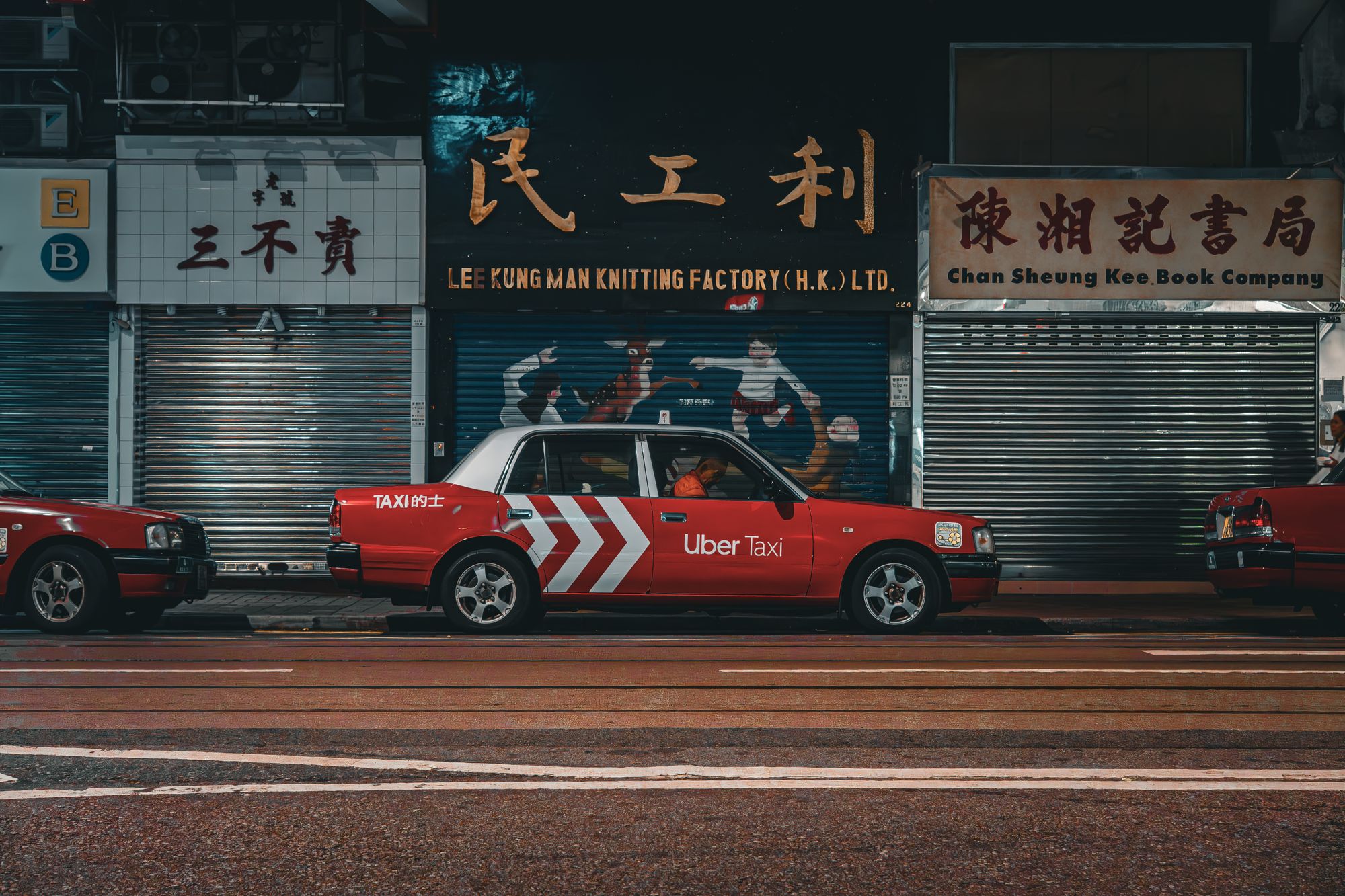 Red Uber Taxi parked on a vibrant Hong Kong city street at night.