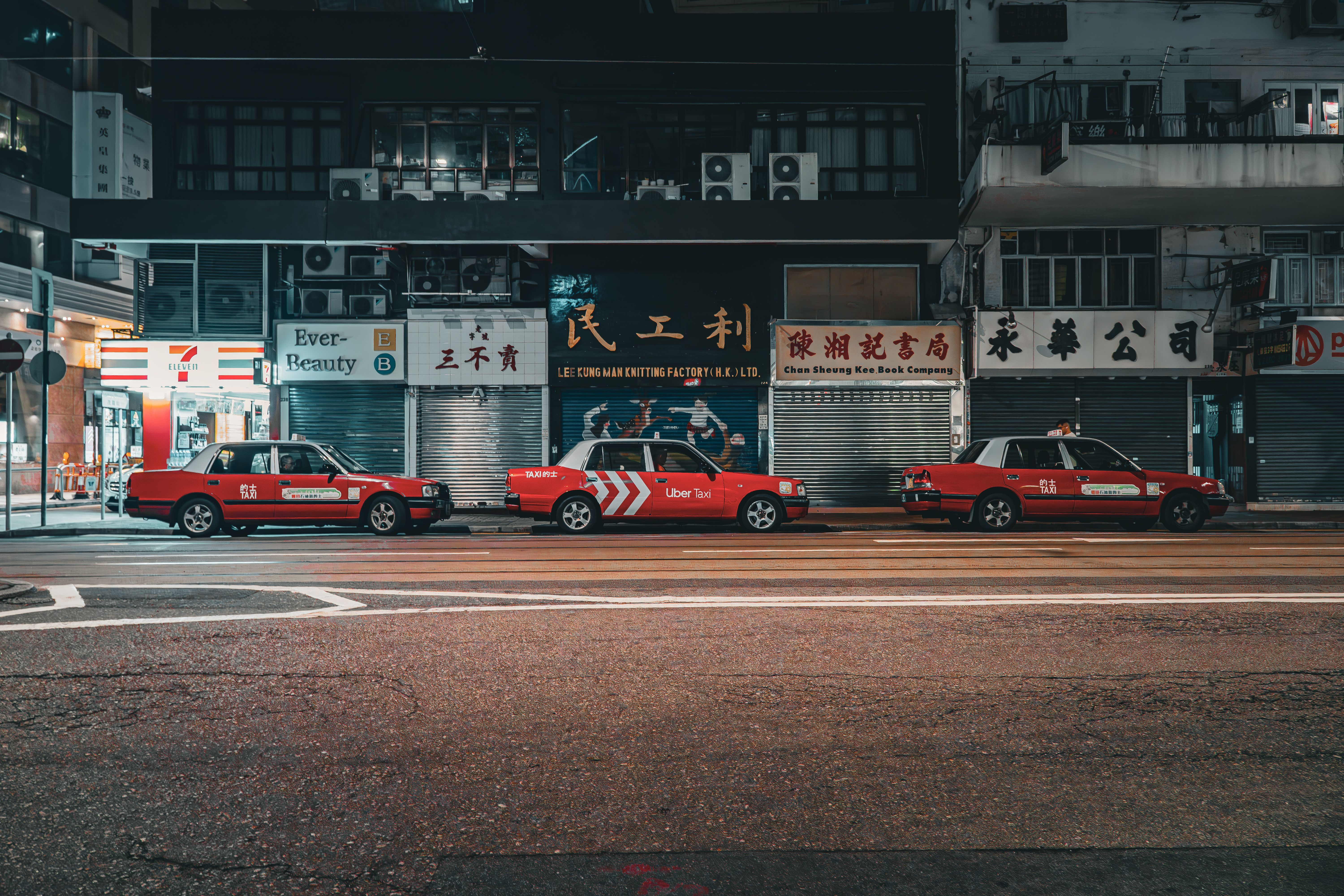 Three red taxis parked on a city street at night in Hong Kong.