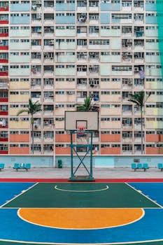 Colorful vertical view of a basketball court against high-rise apartments in Hong Kong, capturing urban lifestyle.