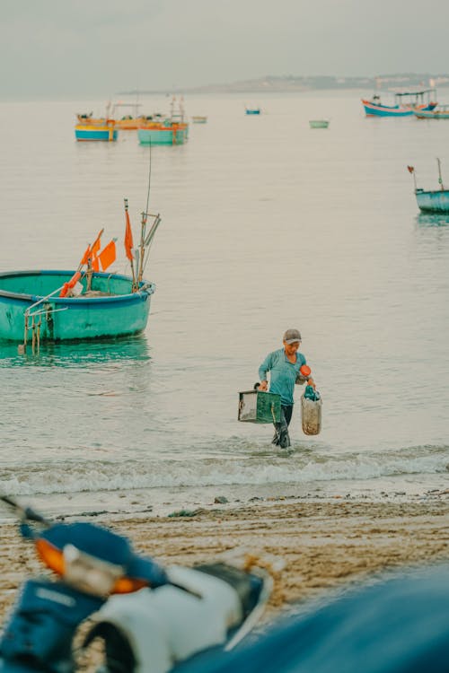 A man walking on the beach with fishing boats