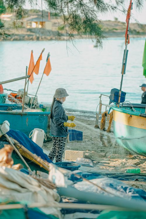 Free A woman standing near fishing boats on Phan Thiet beach, Vietnam, preparing equipment. Stock Photo