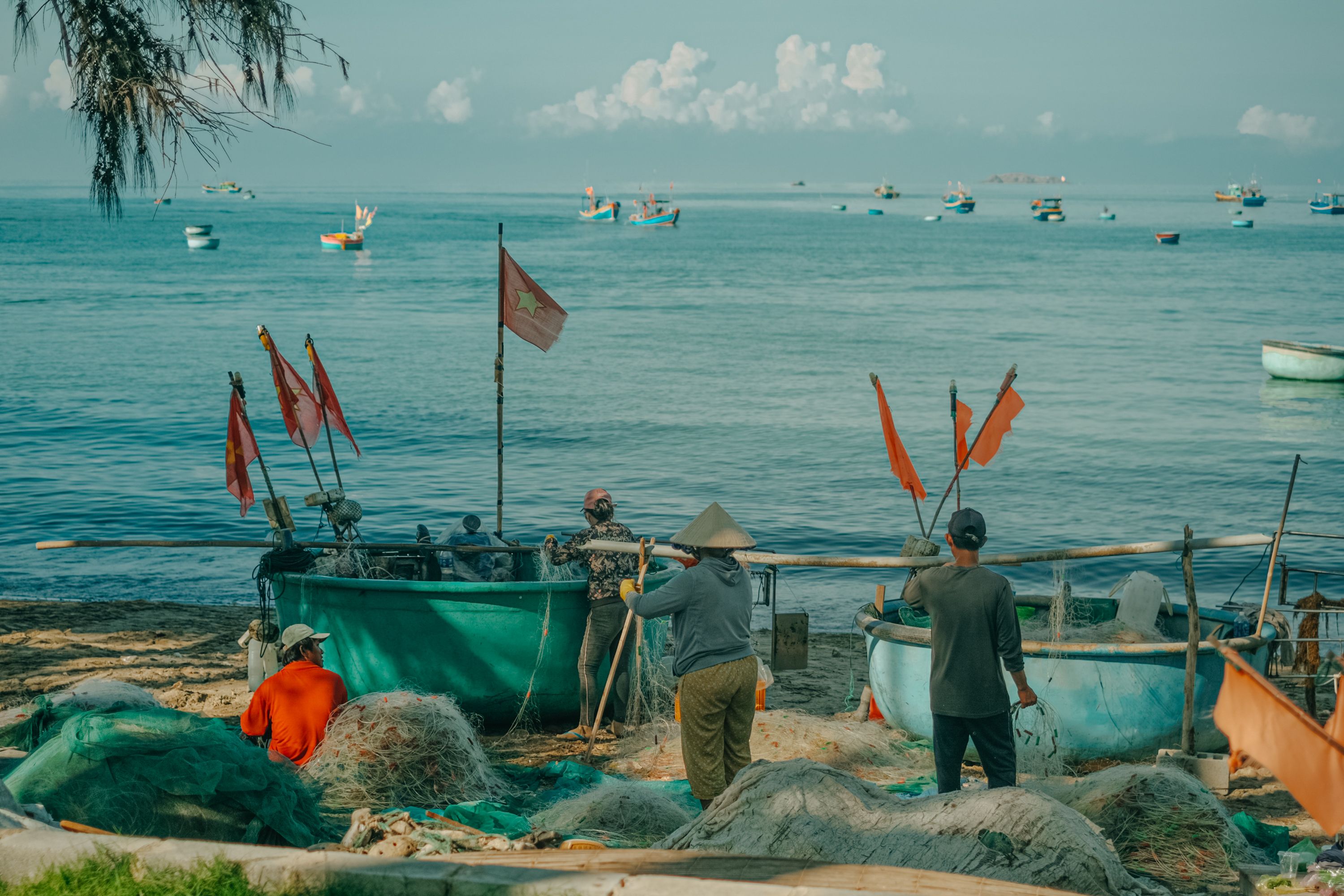 Vietnamese fishermen preparing basket boats on Phan Thiet beach, Bình Thuận, with vibrant sea and sky backdrop.
