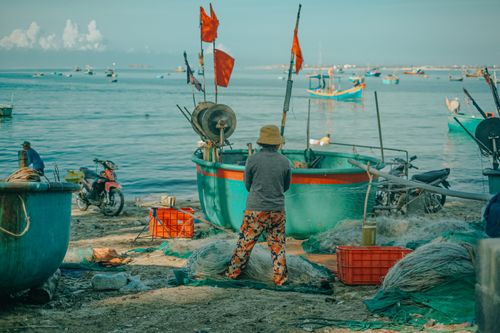 Free Colorful fishing boats and nets in Phan Thiet, Vietnam. A fisherman stands amidst vibrant seaside life. Stock Photo