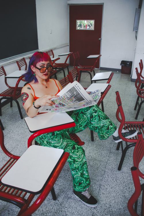 Free Woman with vibrant hair reading a newspaper in a classroom. Stock Photo