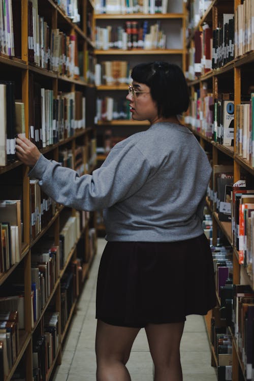 A woman in a skirt and sweater is looking at books in a library