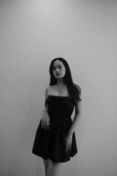 Stylish black and white portrait of a young woman in a black dress against a neutral backdrop.