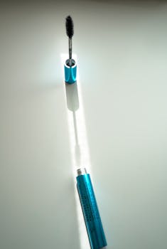 A vertical close-up shot of an open blue mascara tube and brush against a white background.