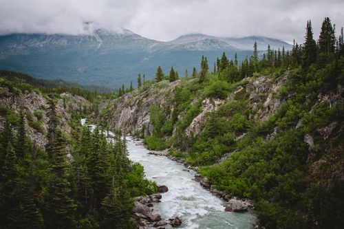 Free Discover the serene natural beauty of a mountain river winding through lush greenery and rugged terrain. Stock Photo