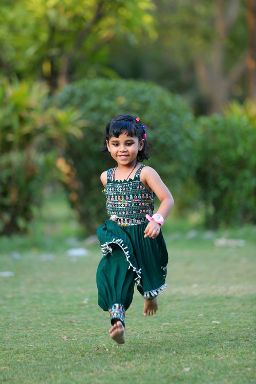 Free A happy child in a colorful outfit runs barefoot on grass in a sunny park, enjoying a carefree moment. Stock Photo
