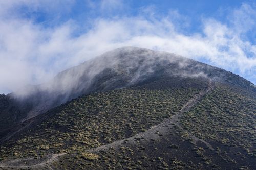Free A remote mountain peak with a cloud veil and rugged trail under a bright sky. Stock Photo