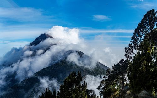 Free Breathtaking view of a mist-covered volcano with lush green trees under a vivid blue sky. Stock Photo