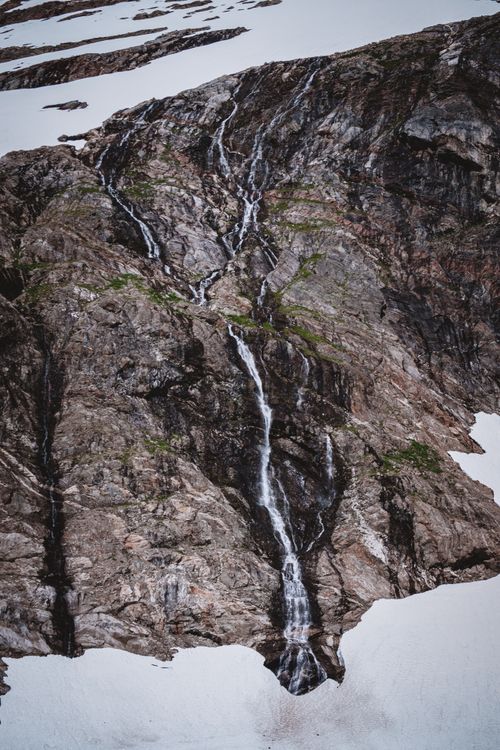 Free A breathtaking waterfall cascades down a rugged rocky terrain in a snowy, glacial landscape. Stock Photo
