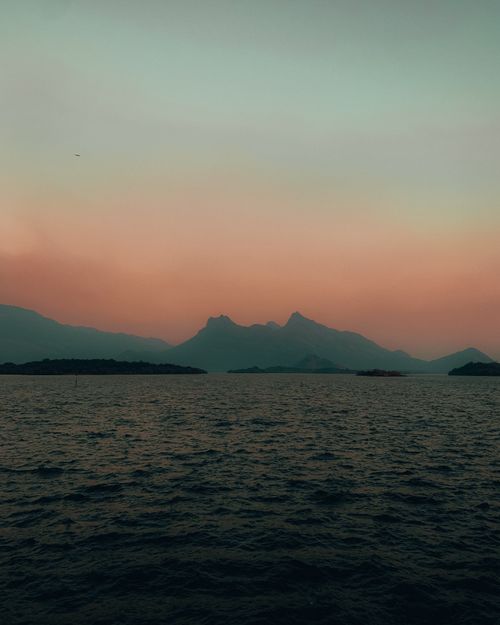 Free Capture the tranquility of dawn with foggy mountains silhouetted over a calm sea. Stock Photo