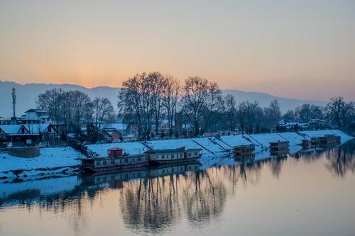 Free Scenic winter view of a snow-covered riverbank with boathouses at sunrise. Stock Photo