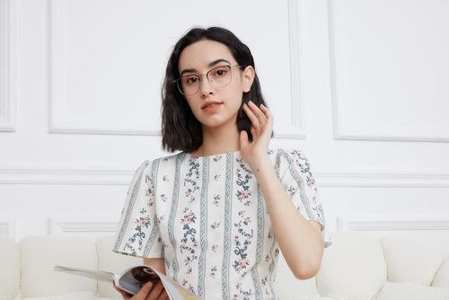Free A stylish woman in glasses and a floral dress reads indoors, showcasing elegance. Stock Photo