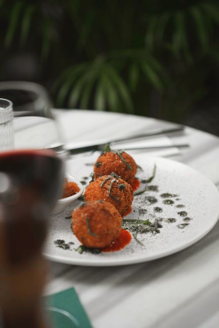 A halved golden-fried arancino on a white plate, showing a creamy saffron-tinted risotto interior with a pull of melted mozzarella and a thin, crackly breadcrumb crust.