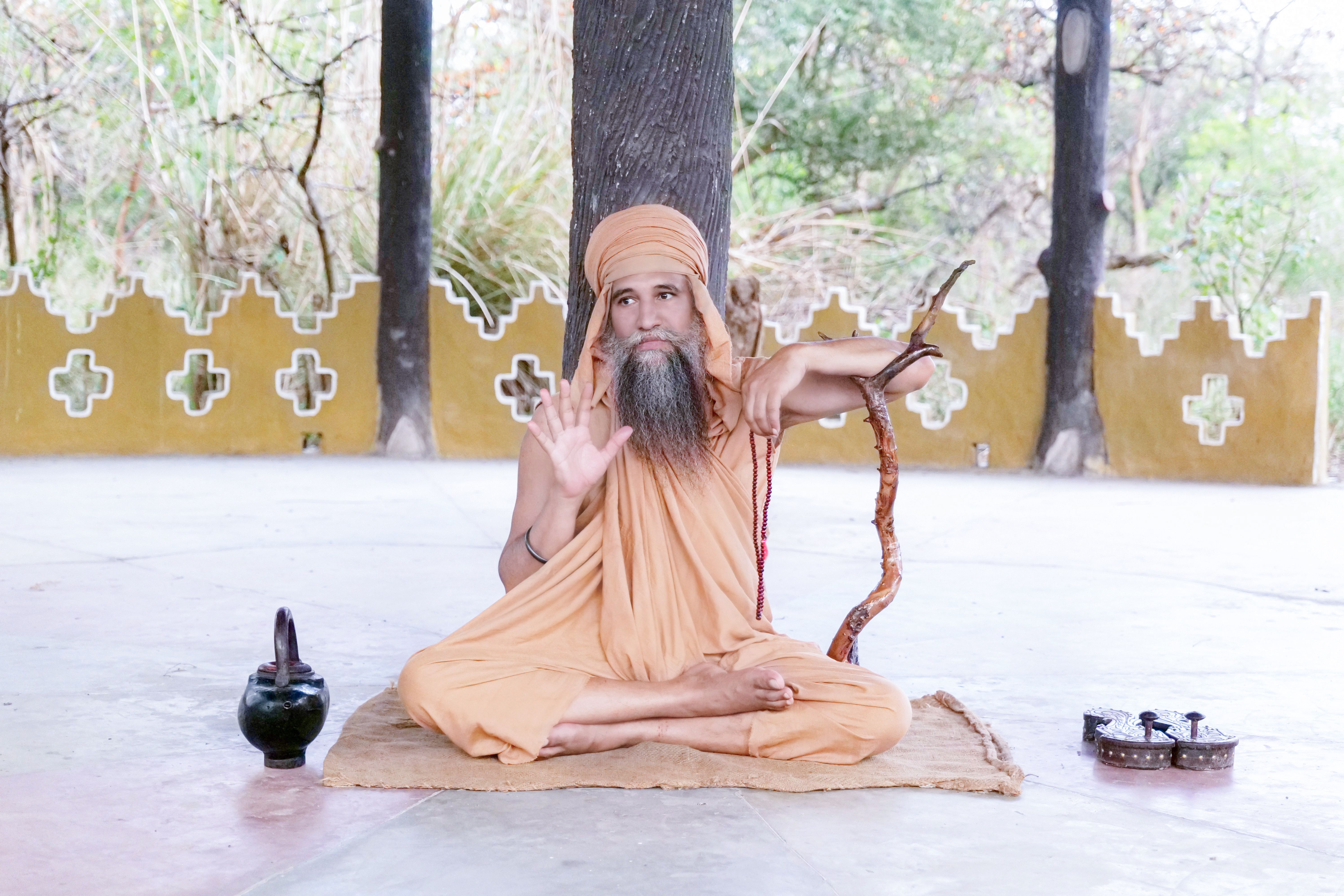 A traditional monk in orange robes meditating outdoors, showcasing Indian culture.