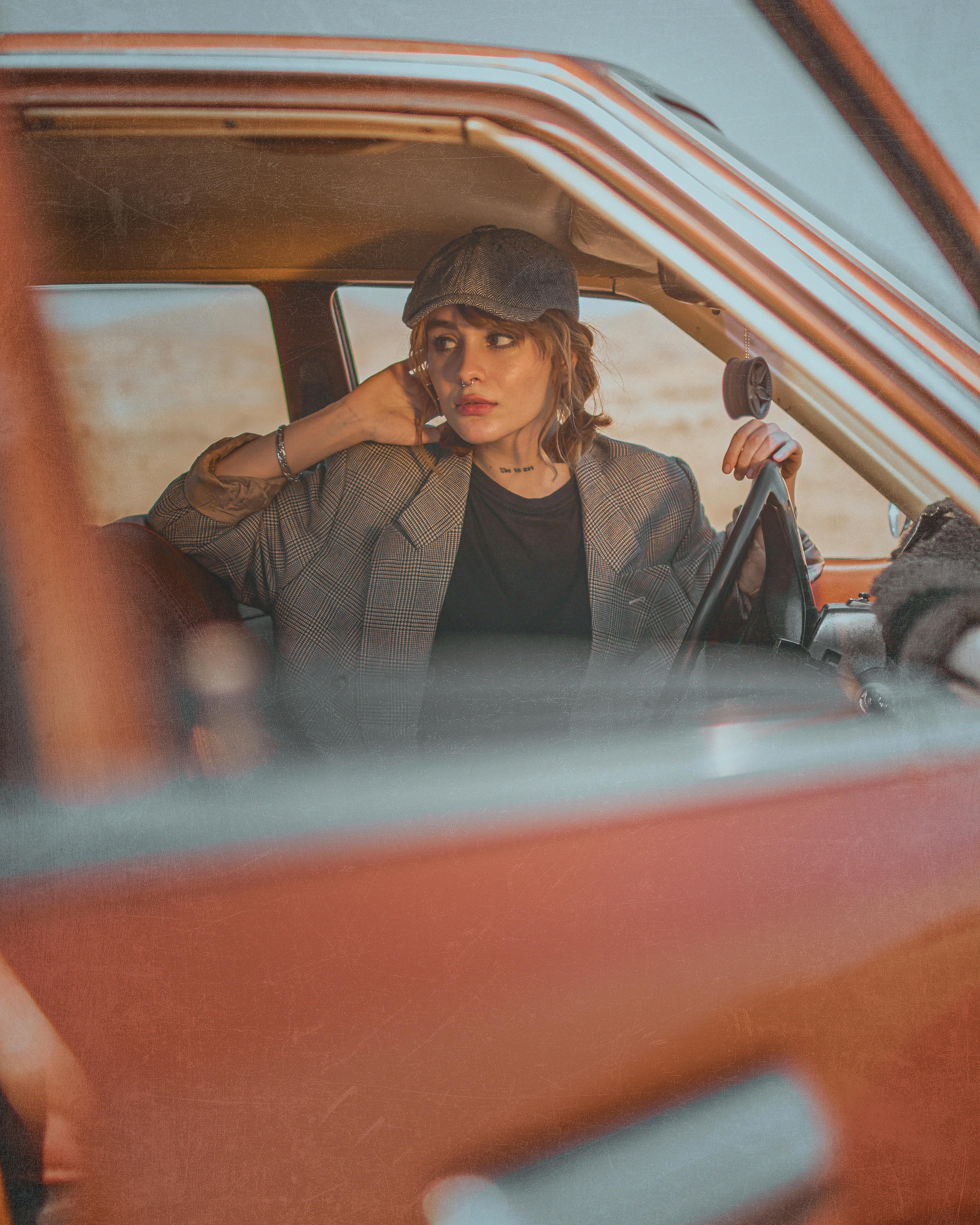 Stylish woman in retro car sitting in a desert landscape, evoking a classic travel vibe.
