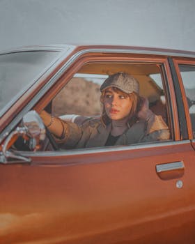 Caucasian woman in vintage car wearing ivy cap, driving through desert landscape.