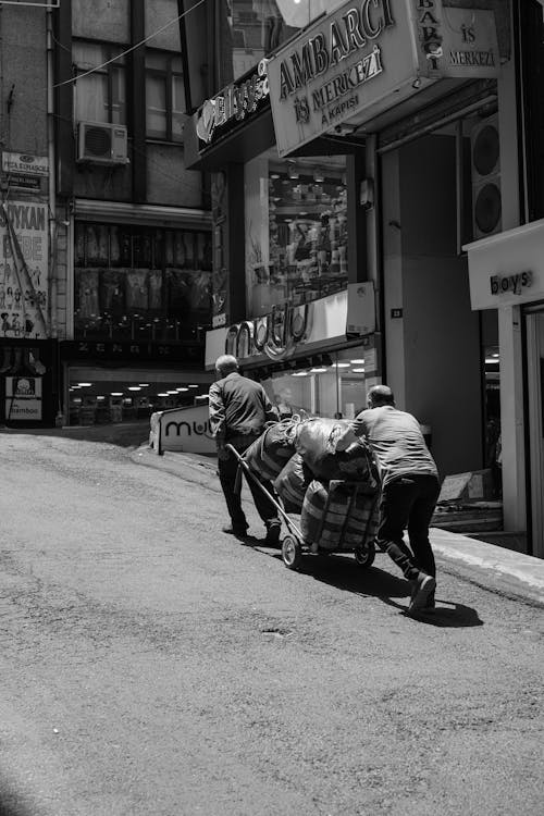 Two men pushing a cart down a street