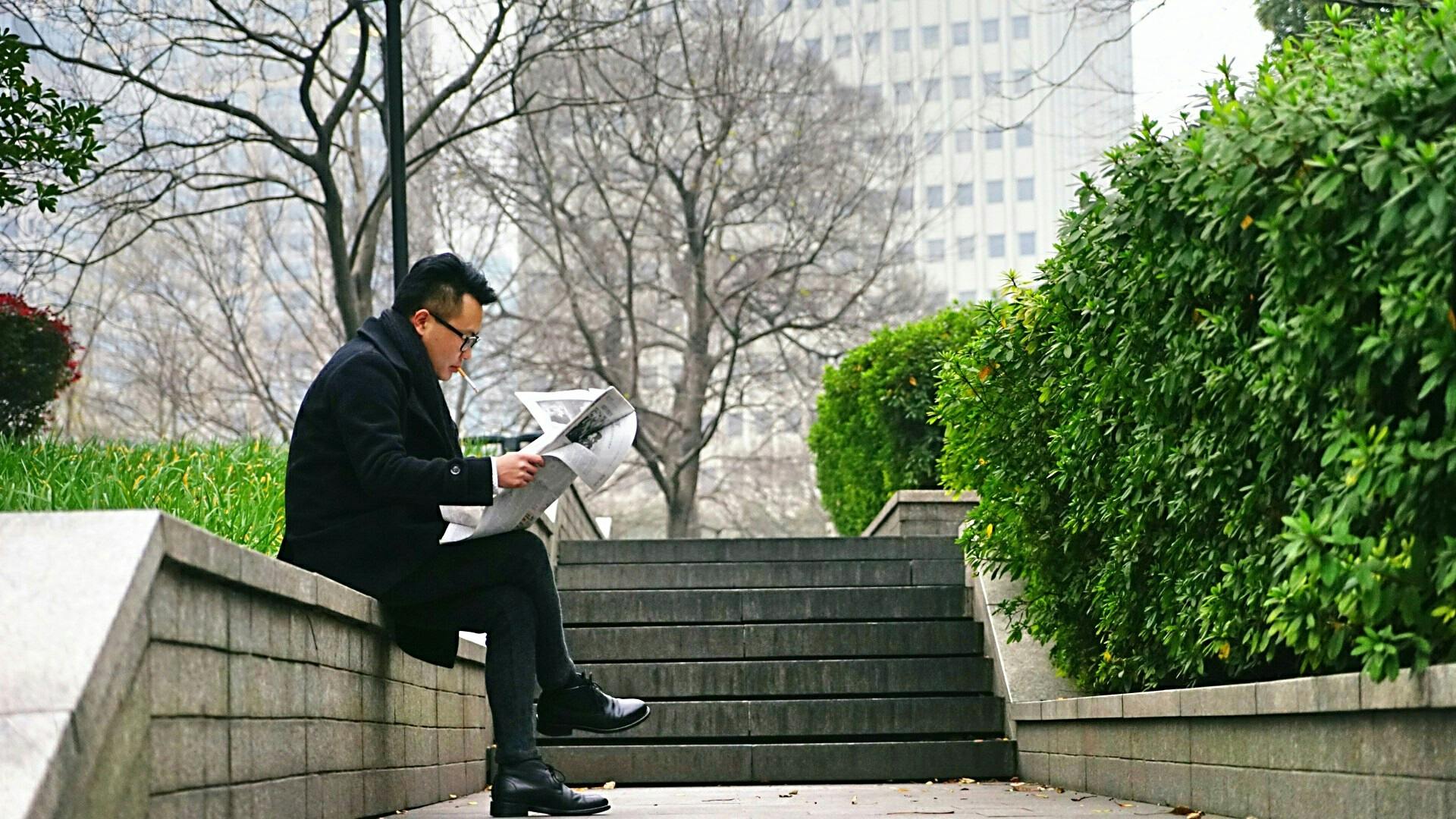 man reading newspaper sitting on stair wall