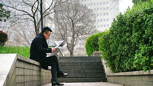 Free Man Reading Newspaper Sitting on Stair Wall Stock Photo