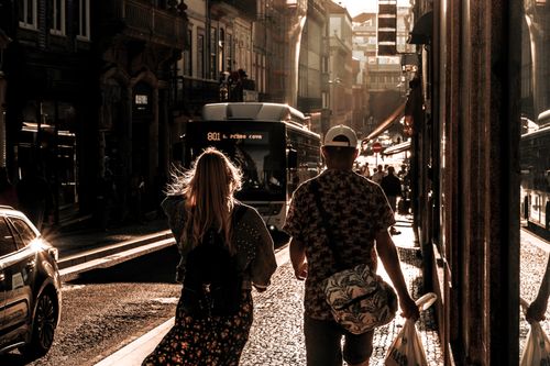 Free A couple strolls through Porto, Portugal, on a bustling city street during sunset. Stock Photo