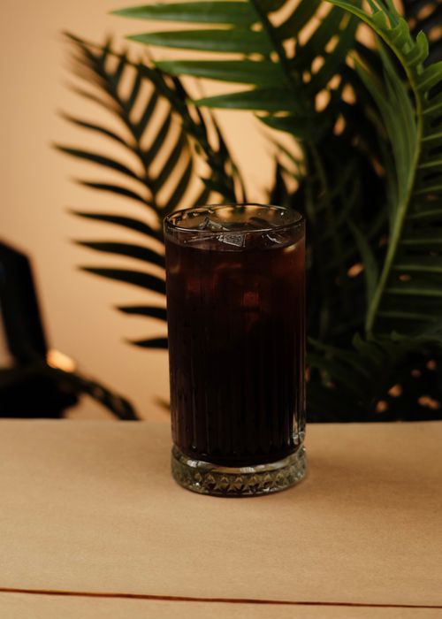 Free A glass of iced coffee sits refreshingly against a lush tropical backdrop of palm leaves. Stock Photo