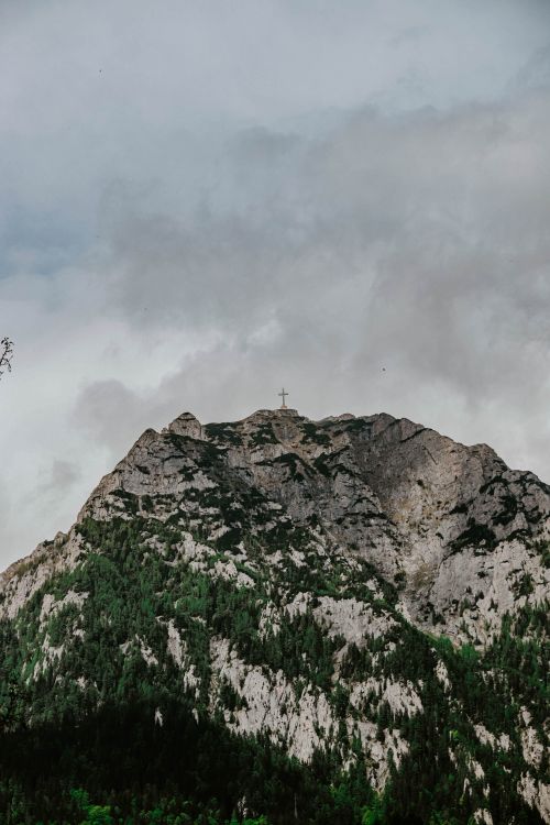 Free Stunning mountain landscape with a cross atop the peak against a moody, cloudy sky. Stock Photo