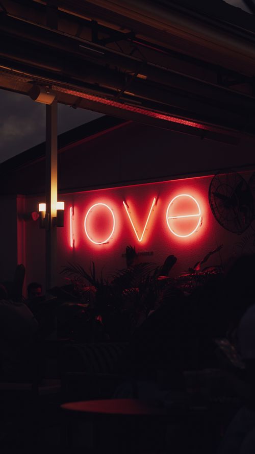 Free Moody neon 'love' sign glowing in a dark outdoor café, evoking romance. Stock Photo