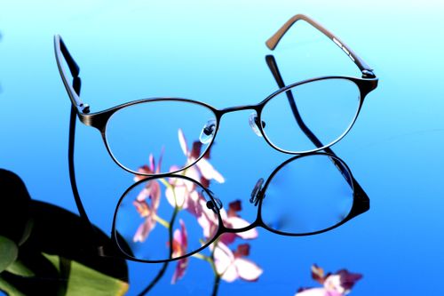 Free Stylish eyeglasses on reflective surface with orchid blossoms. Perfect for design inspiration. Stock Photo