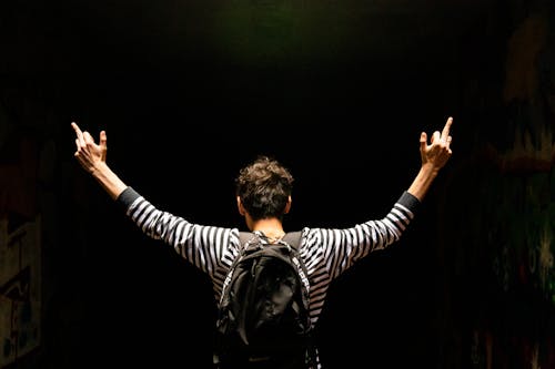 Back View Of Man Carrying A Backpack With Arms Raised Doing The Middle Finger