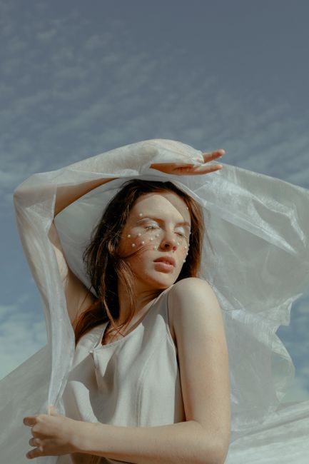 Artistic portrait of a woman outdoors with white fabric and soft lighting.