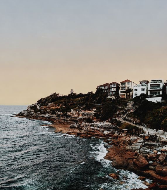 Beautiful coastal homes on a rocky cliff with ocean view at dusk.