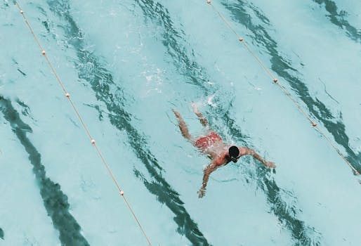 A person swimming in an outdoor pool with clear blue water, seen from above. Perfect for summer and fitness themes.