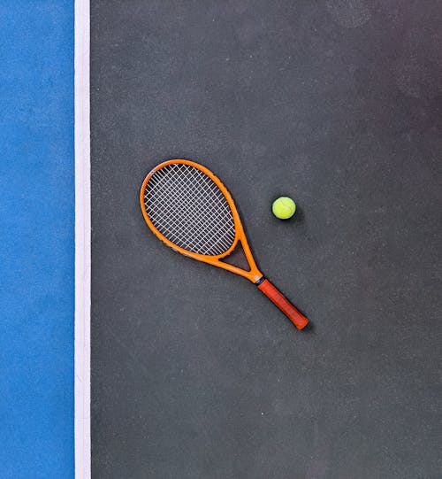 Raqueta De Tenis Naranja Al Lado De Una Pelota De Tenis Verde