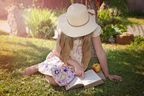 Woman Sitting on Grass While Reading Book