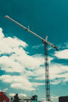 一台高耸的建筑起重机映衬在生机勃勃的蓝天下，云层散落，象征着城市的发展