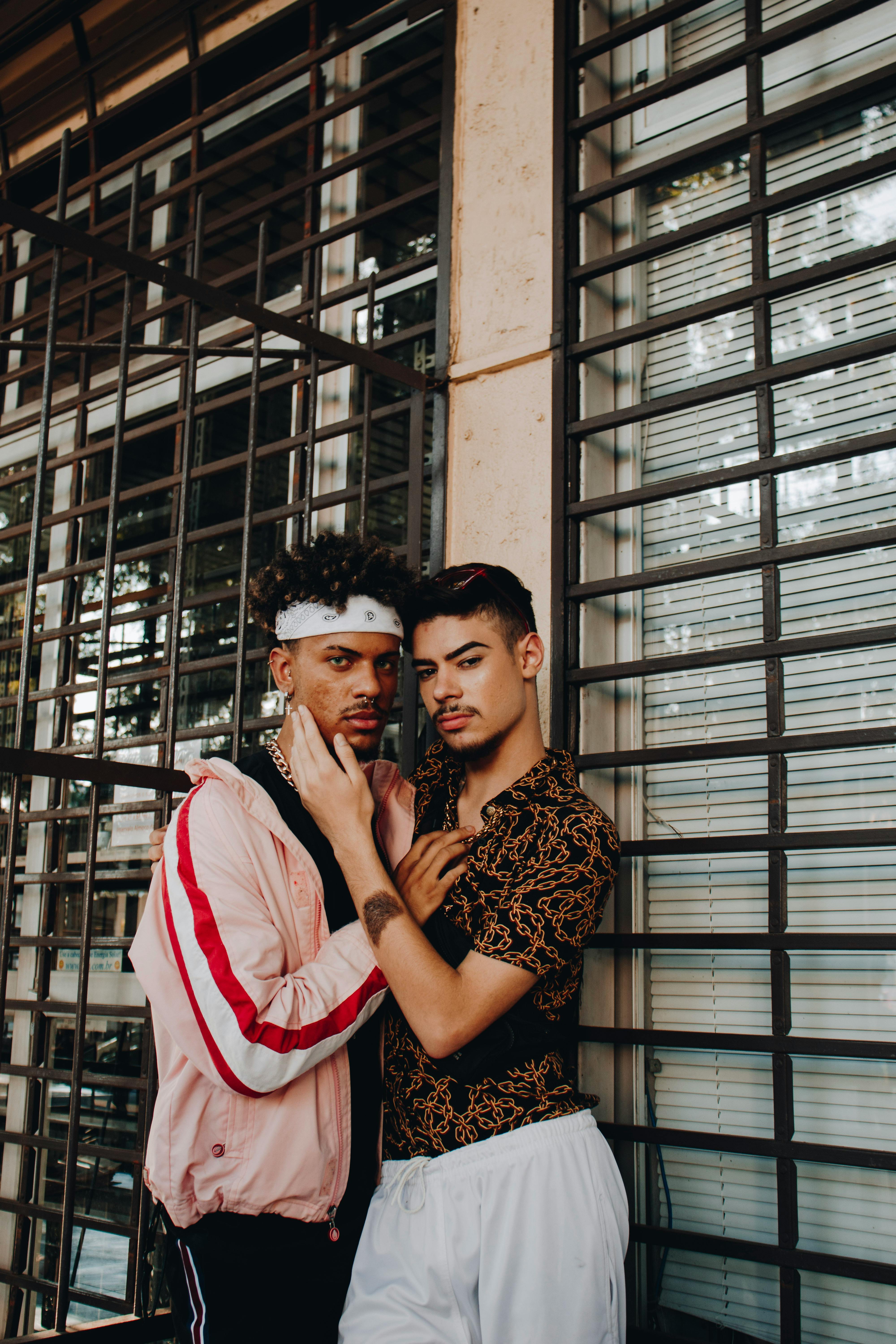 two men posing beside a metal grill while holding each other