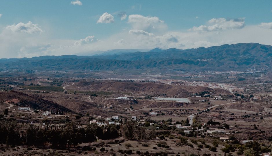 Impresionante vista aérea de un paisaje rural con montañas al fondo bajo un brillante cielo azul.