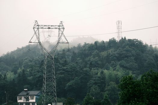 A misty forest landscape with a towering transmission tower and distant architecture, blending nature and industry.