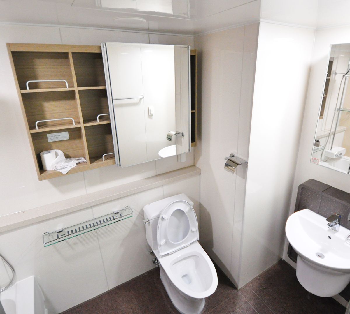 Freestanding over the toilet cabinet with shelves holding towels and toiletries in a minimalist bathroom