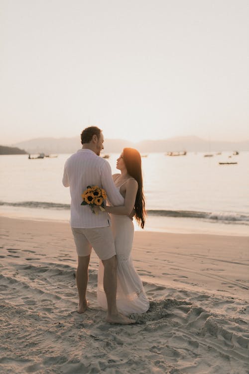 A bride and groom standing on the beach at sunset