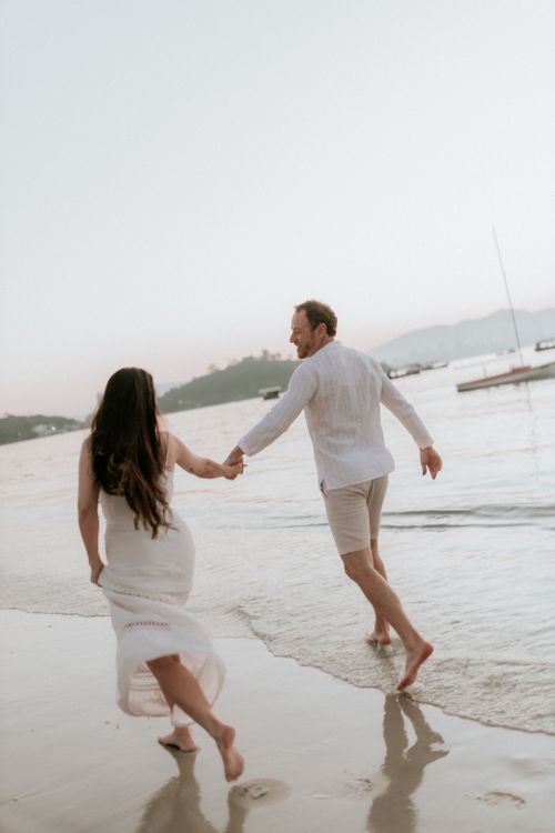 Free A couple running hand in hand on a beach during sunset, symbolizing love and freedom. Stock Photo