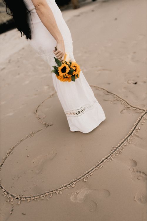 Free Woman holding sunflowers on a beach with a heart drawn in the sand. Stock Photo