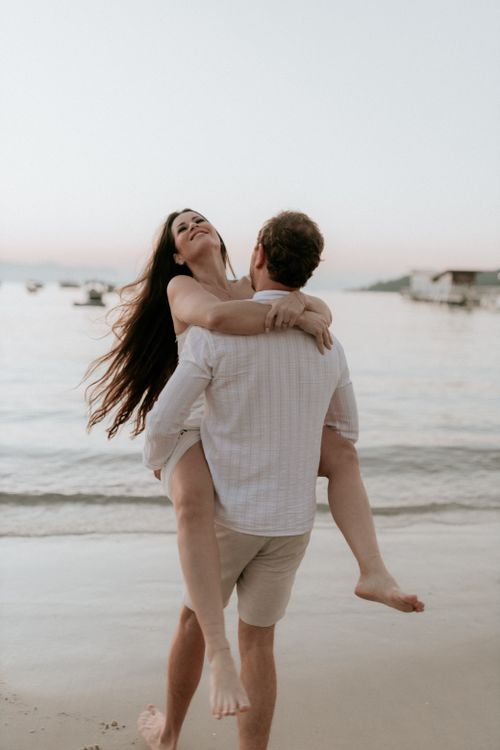 Free A joyful couple embraces on a serene beach, showcasing love and happiness at sunset. Stock Photo