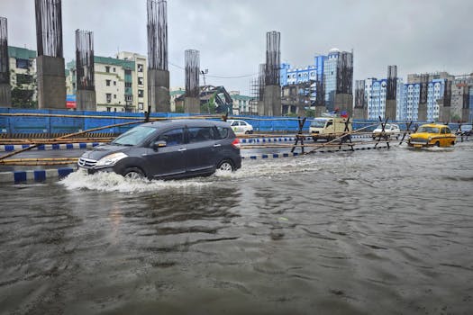 Cars navigate a flooded street in Kolkata, India, amidst heavy rain and overcast skies.